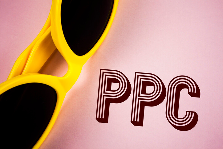 Yellow sunglasses on a pink background alongside PPC that is written next to the sunglasses